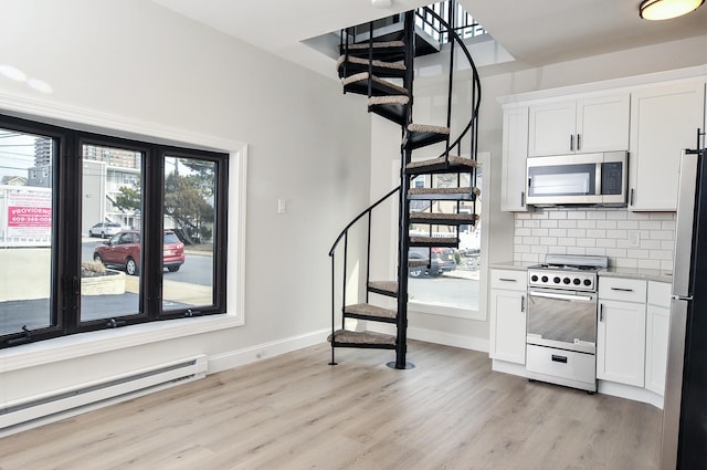 kitchen featuring stainless steel appliances, light wood finished floors, baseboard heating, and a wealth of natural light