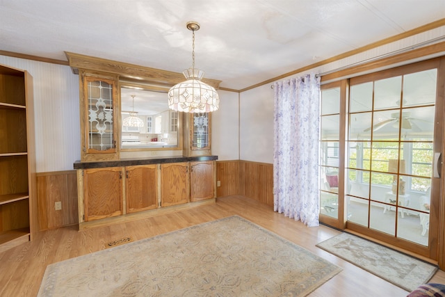 unfurnished dining area with wooden walls, a notable chandelier, wainscoting, light wood finished floors, and ornamental molding