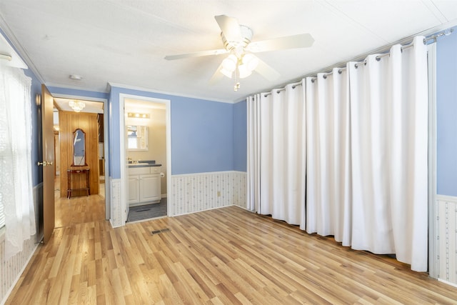 unfurnished bedroom with ornamental molding, wainscoting, light wood finished floors, and ceiling fan