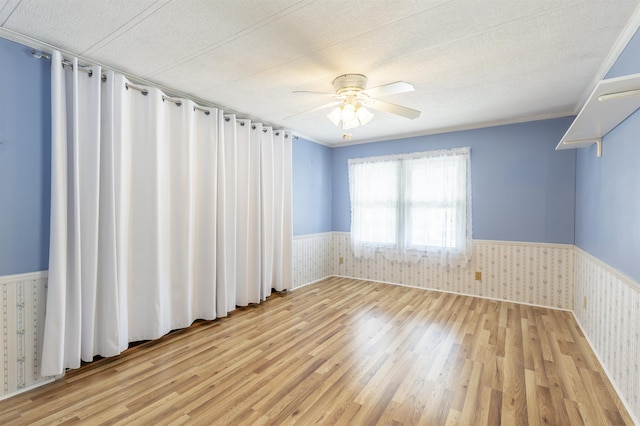 spare room with a ceiling fan, light wood finished floors, and a wainscoted wall