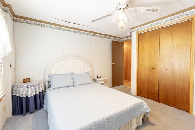 bedroom featuring a ceiling fan, light colored carpet, ornamental molding, and a closet