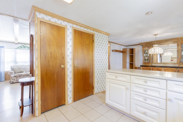 kitchen featuring crown molding, wallpapered walls, light countertops, white cabinetry, and decorative light fixtures