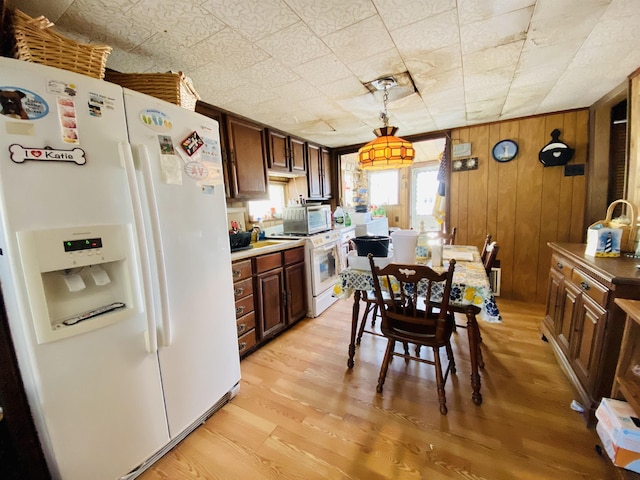 kitchen with pendant lighting, white appliances, wooden walls, and light hardwood / wood-style flooring