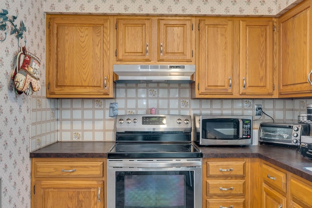 kitchen featuring dark countertops, under cabinet range hood, stainless steel appliances, and wallpapered walls