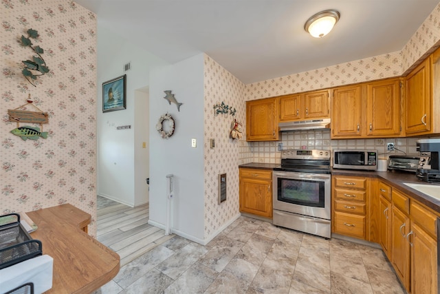 kitchen featuring stainless steel appliances, dark countertops, under cabinet range hood, and wallpapered walls