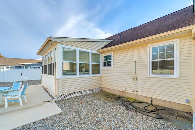 view of home's exterior featuring a patio, a shingled roof, fence, and a sunroom