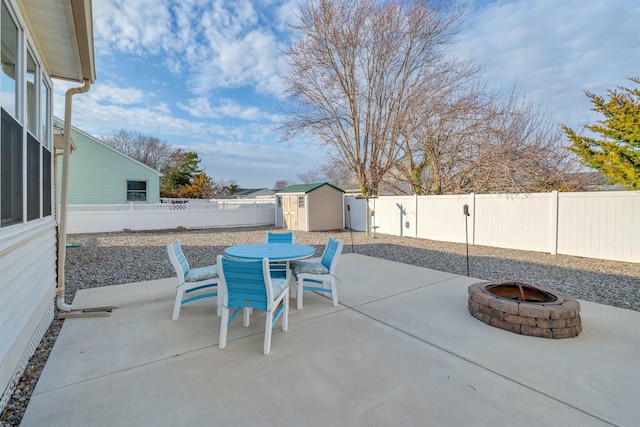 view of patio featuring an outdoor fire pit, a fenced backyard, an outbuilding, a storage unit, and outdoor dining space