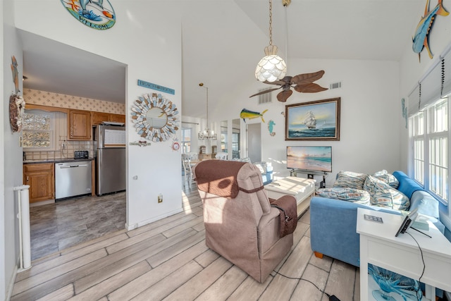 living area featuring ceiling fan with notable chandelier, high vaulted ceiling, light wood finished floors, and visible vents