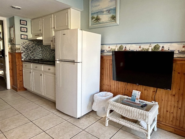 kitchen featuring backsplash, freestanding refrigerator, light tile patterned flooring, white cabinets, and under cabinet range hood