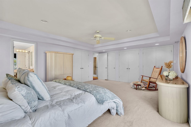 bedroom featuring ceiling fan, two closets, carpet, and a tray ceiling