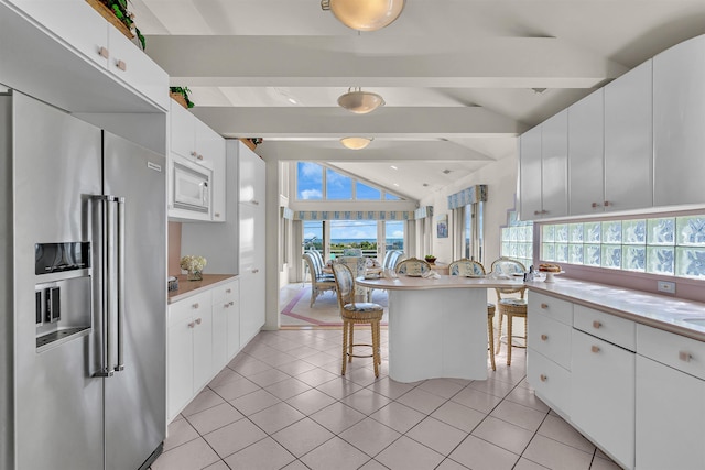 kitchen featuring white microwave, high end fridge, light tile patterned flooring, and vaulted ceiling with beams