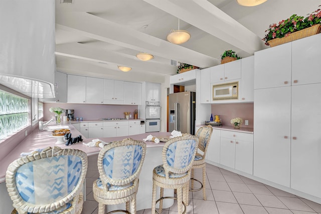 kitchen with beam ceiling, stainless steel appliances, a peninsula, light countertops, and light tile patterned floors