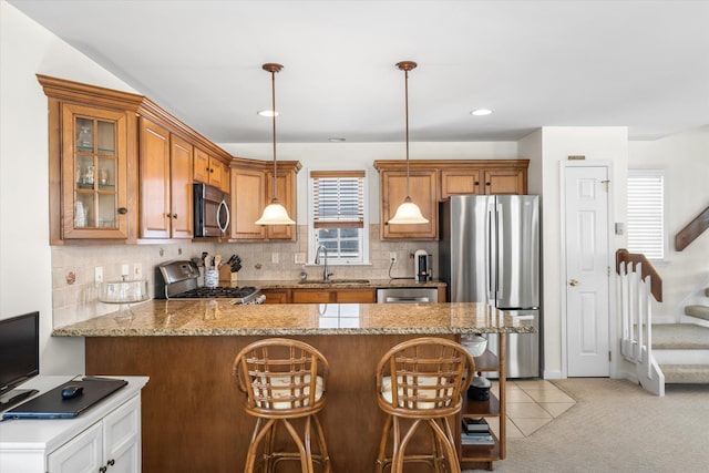 kitchen featuring brown cabinetry, a peninsula, a sink, stainless steel appliances, and backsplash