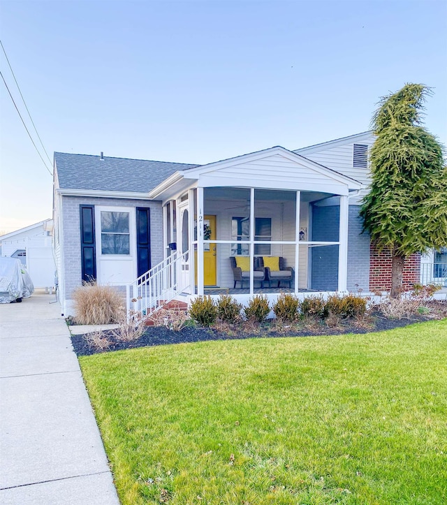 view of front of property with covered porch, roof with shingles, a front lawn, and brick siding