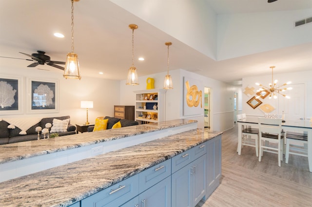 kitchen with light stone counters, visible vents, light wood-style floors, open floor plan, and decorative light fixtures