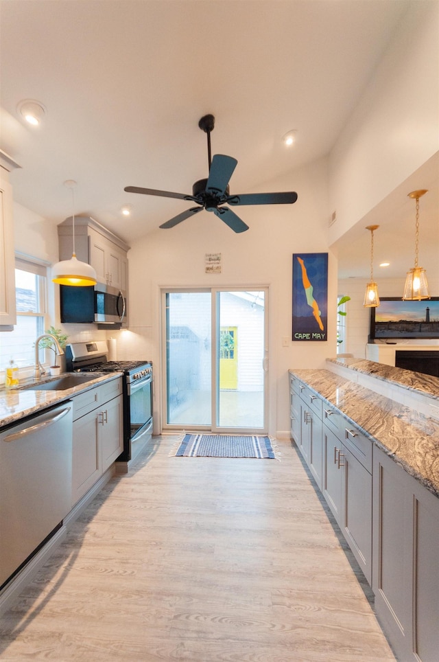 kitchen with hanging light fixtures, light wood-style flooring, stainless steel appliances, and a sink