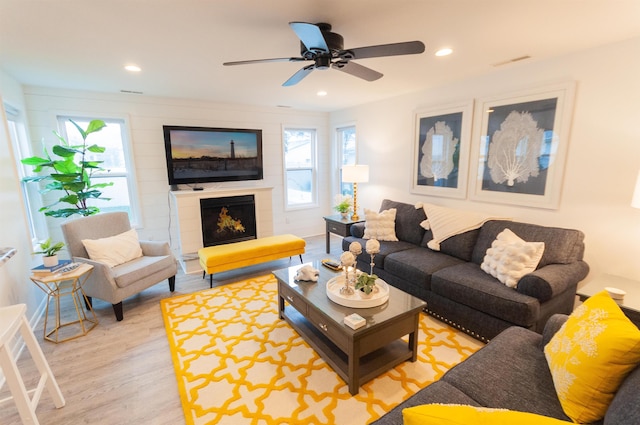 living room featuring a warm lit fireplace, visible vents, a ceiling fan, light wood-style flooring, and recessed lighting