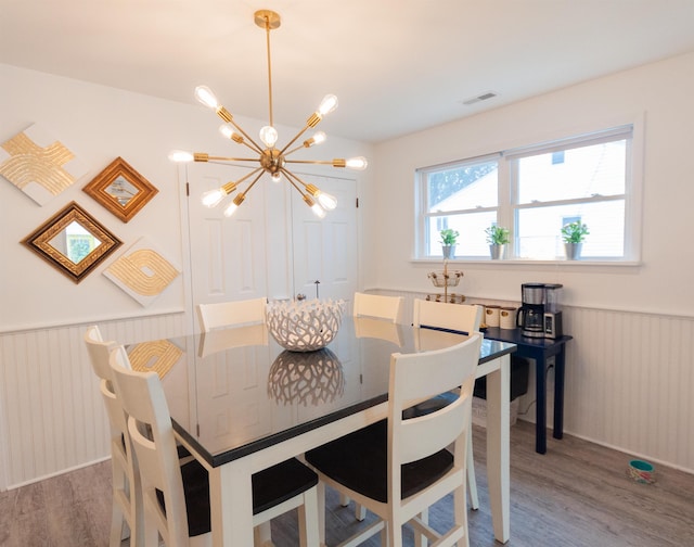 dining area with an inviting chandelier, visible vents, wood finished floors, and wainscoting