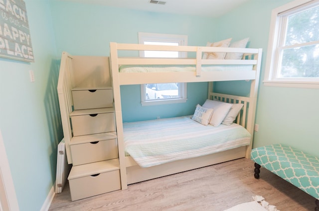 bedroom featuring baseboards, radiator heating unit, visible vents, and wood finished floors