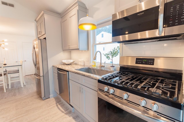 kitchen featuring light stone counters, stainless steel appliances, tasteful backsplash, visible vents, and a sink