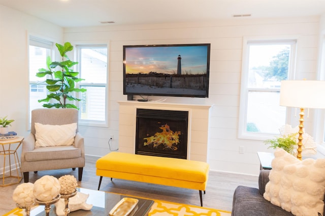 living area with baseboards, visible vents, a fireplace with raised hearth, and wood finished floors