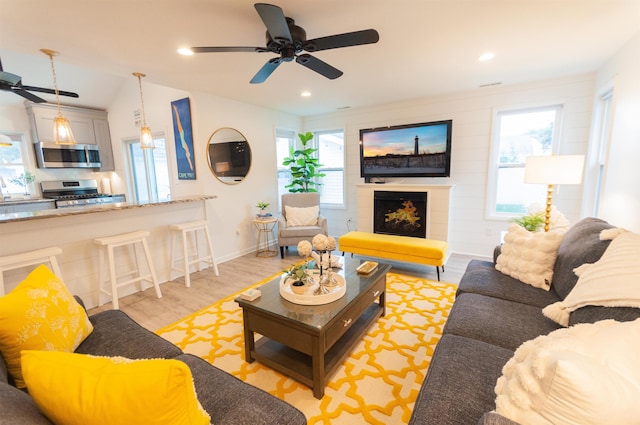 living area featuring a large fireplace, light wood finished floors, baseboards, ceiling fan, and recessed lighting