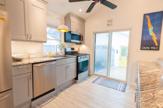 kitchen featuring light stone counters, tasteful backsplash, appliances with stainless steel finishes, vaulted ceiling, and light wood-type flooring