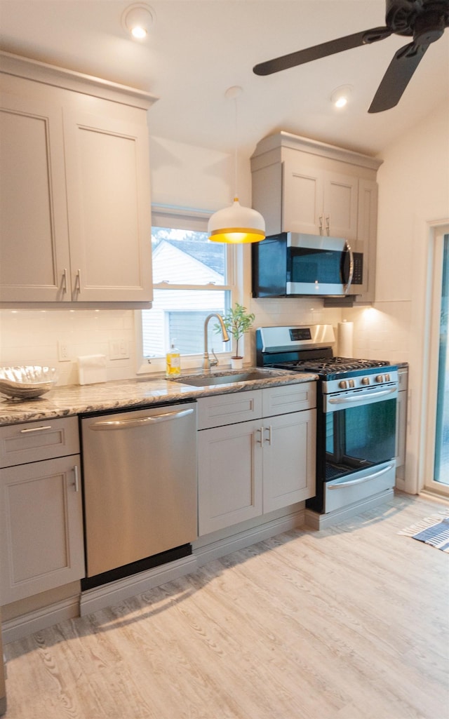 kitchen with stainless steel appliances, light wood-type flooring, a sink, and pendant lighting