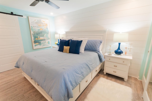 bedroom with a ceiling fan, light wood-style flooring, and a barn door