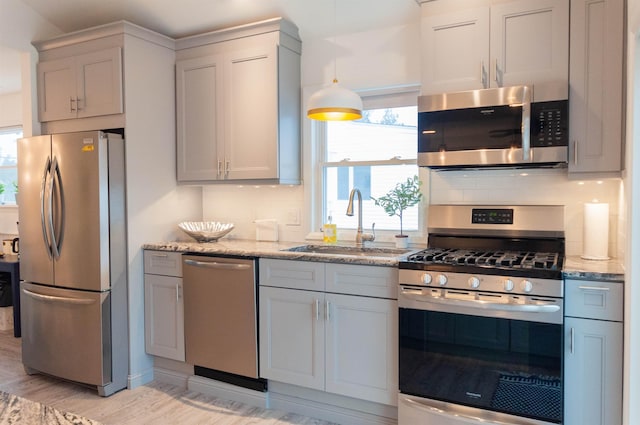 kitchen with light stone counters, light wood finished floors, decorative backsplash, appliances with stainless steel finishes, and a sink