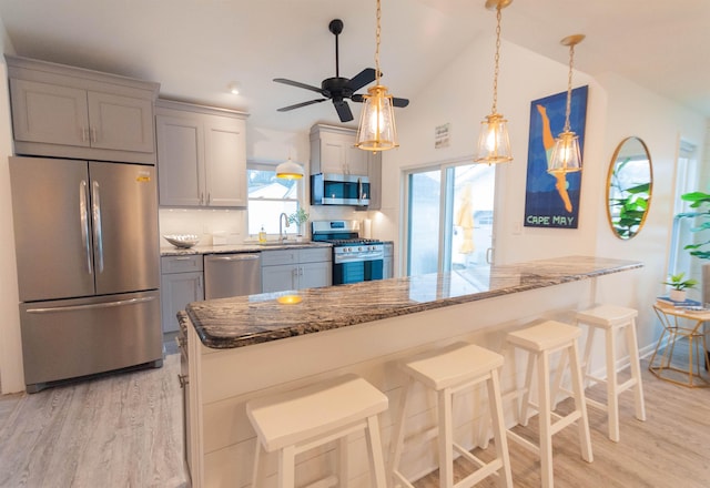 kitchen featuring appliances with stainless steel finishes, stone countertops, vaulted ceiling, a sink, and light wood-type flooring