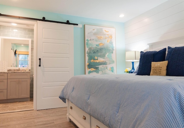 bedroom featuring light wood-type flooring, a sink, ensuite bathroom, and a barn door