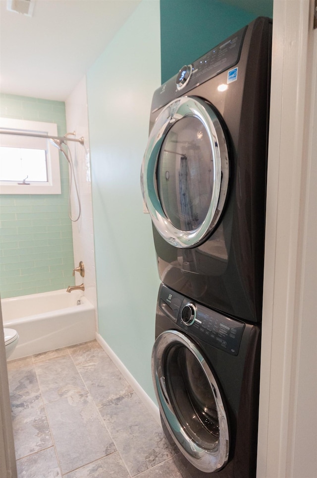 clothes washing area featuring laundry area, stacked washer / dryer, and baseboards