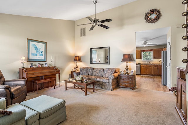 living area with a towering ceiling, light carpet, a ceiling fan, and visible vents
