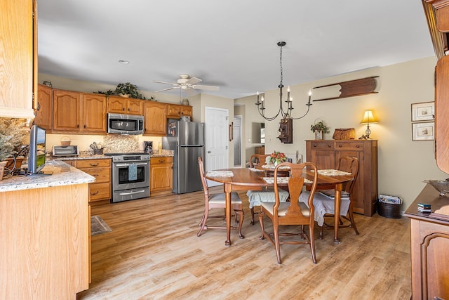 kitchen featuring decorative backsplash, light wood finished floors, ceiling fan with notable chandelier, and stainless steel appliances