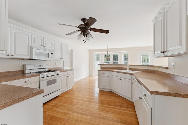 kitchen with white appliances, a peninsula, a sink, white cabinetry, and light wood-type flooring