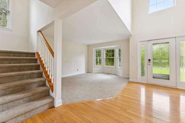 foyer with crown molding, baseboards, stairway, hardwood / wood-style floors, and a high ceiling