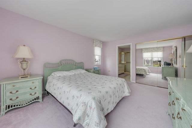 bedroom with connected bathroom, light carpet, multiple windows, and a closet