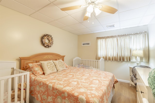 bedroom featuring ceiling fan, a paneled ceiling, wood finished floors, visible vents, and baseboards