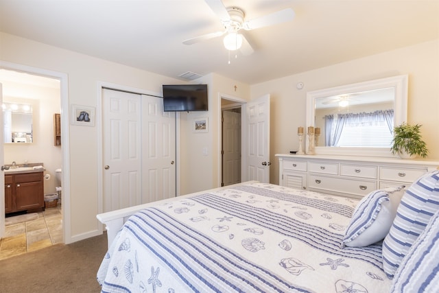 bedroom with a closet, light colored carpet, a ceiling fan, a sink, and ensuite bath