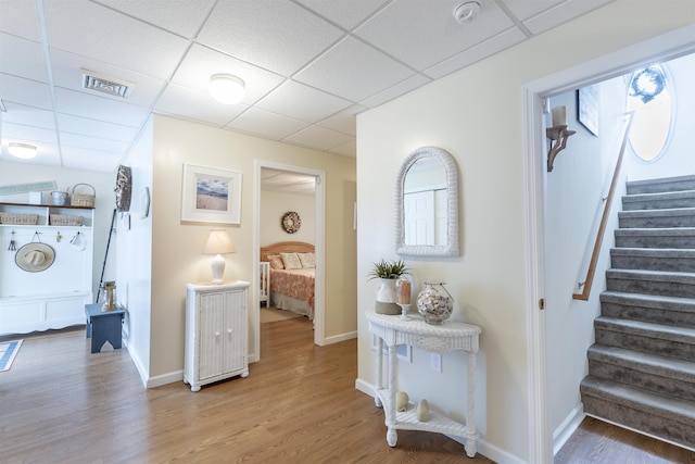 hallway featuring a paneled ceiling, visible vents, stairway, and wood finished floors