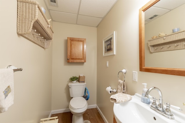 bathroom featuring visible vents, toilet, wood finished floors, a paneled ceiling, and a sink