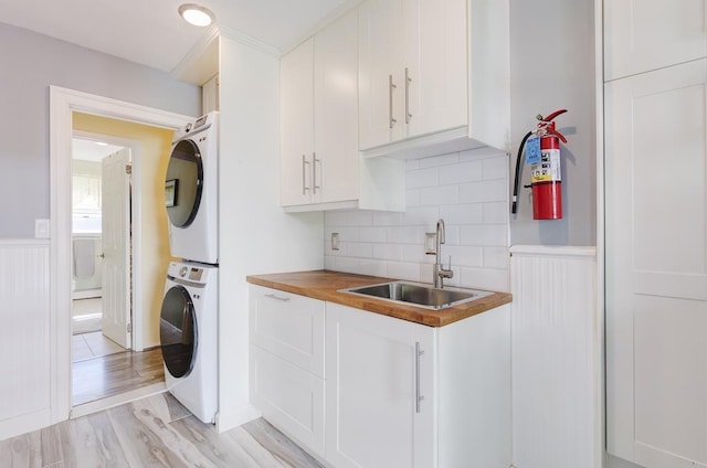 kitchen with white cabinetry, sink, stacked washer / drying machine, and light hardwood / wood-style flooring