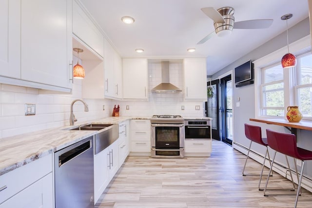 kitchen with stainless steel appliances, wall chimney range hood, pendant lighting, a baseboard radiator, and white cabinetry