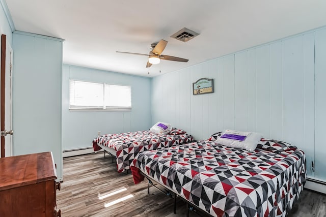 bedroom featuring hardwood / wood-style floors, ceiling fan, baseboard heating, and wooden walls