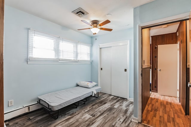 bedroom with hardwood / wood-style floors, a closet, baseboard heating, and ceiling fan