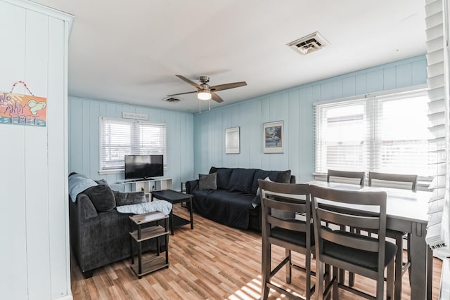 living room with ceiling fan, light wood-type flooring, and wooden walls