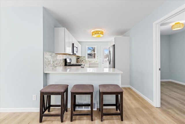 kitchen with light wood-type flooring, a kitchen breakfast bar, tasteful backsplash, stainless steel appliances, and light countertops