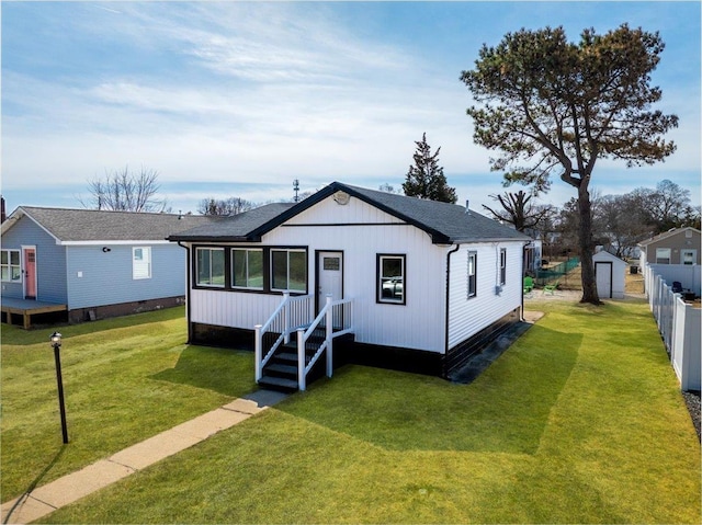 view of front of house with roof with shingles, a front yard, and fence