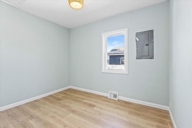 spare room with electric panel, visible vents, light wood-type flooring, and baseboards